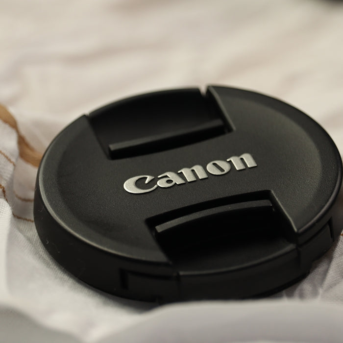 a canon lens cap sitting on top of a white blanket